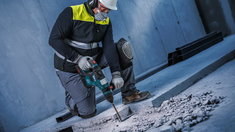 Una persona que usa equipo de seguridad utiliza un martillo rotatorio para romper hormigón.