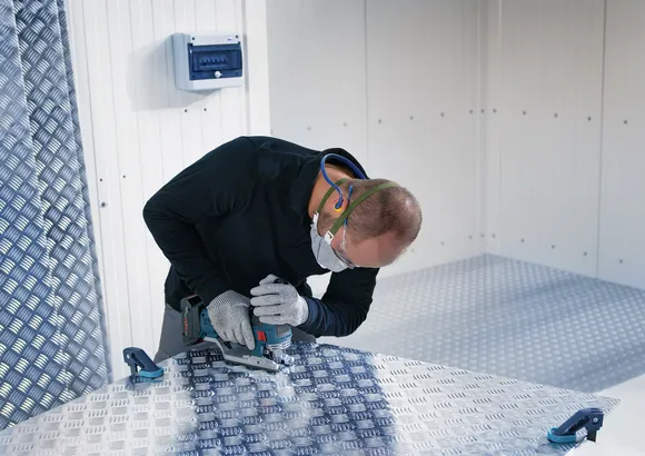 Una persona que usa equipo de seguridad utiliza una sierra caladora para cortar una lámina de metal.