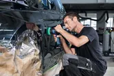 Una persona que usa equipo de seguridad pule la puerta de un automóvil con una herramienta inalámbrica.