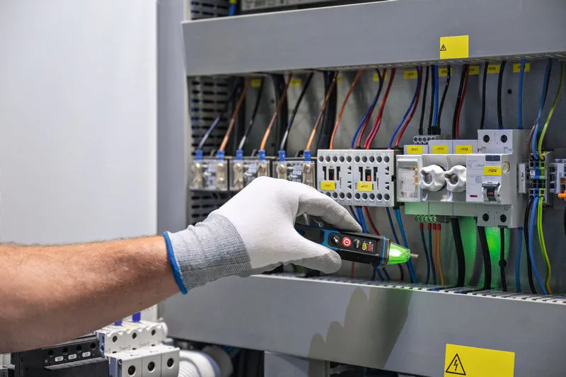 Una persona que usa equipo de seguridad prueba los cables del panel eléctrico con un detector de voltaje.