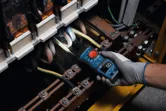 Una persona que usa equipo de seguridad utiliza un medidor de horquilla para probar cables eléctricos en un panel.