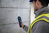 Una persona que usa equipo de seguridad utiliza un medidor de humedad del material para comprobar una pared de hormigón.