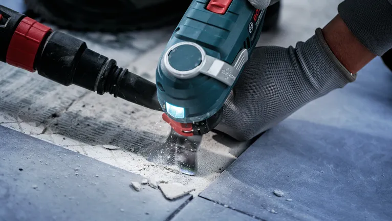 Una persona que usa equipo de seguridad utiliza una herramienta eléctrica para cortar baldosas.