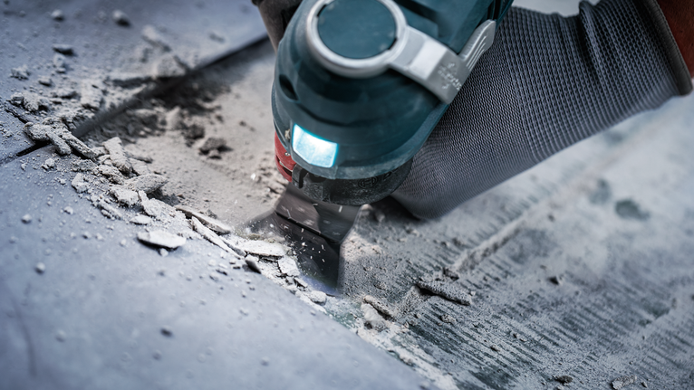 Persona que usa equipo de seguridad y utiliza una herramienta múltiple para retirar material de un piso.