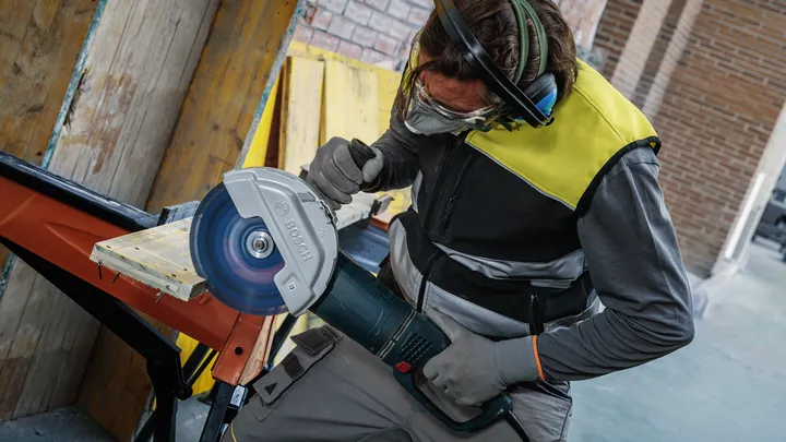Una persona que usa equipo de seguridad corta una tabla de madera con una sierra circular grande.