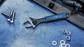 Una llave inglesa ajustable yace sobre una superficie de trabajo junto a tornillos, arandelas y tuercas.