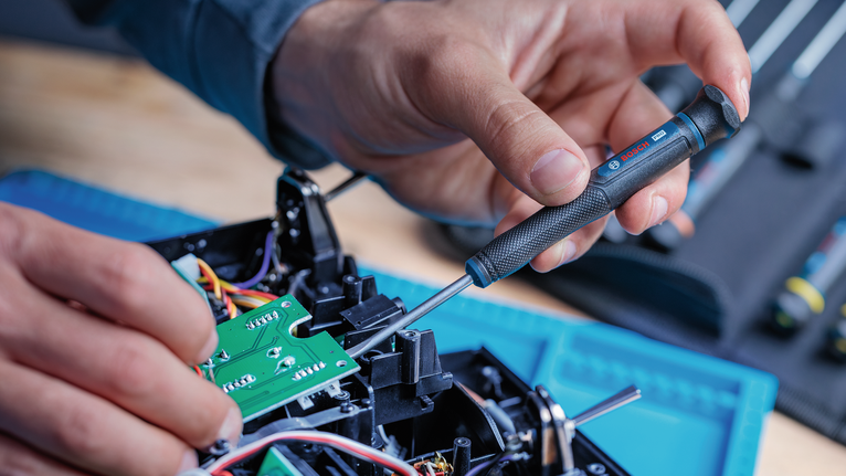 Persona que utiliza un destornillador de precisión para ensamblar placas de circuitos electrónicos.