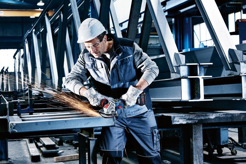 Turvavarustust kandev inimene lihvib akuga nurklihvijaga metalltalasid.