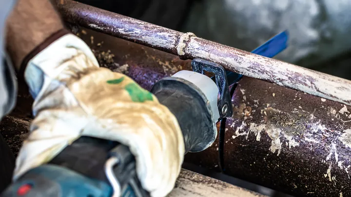 Turvavarustust kandev inimene lõikab roostes metalltoru edasi-tagasi liikuva saega.