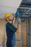 Turvavarustust kandev inimene kinnitab elektrilise tööriista abil kipsplaati laeraami külge.