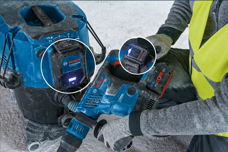 Kaitsevarustust kandev inimene kasutab tolmuimejasüsteemiga ühendatud elektrilist tööriista.