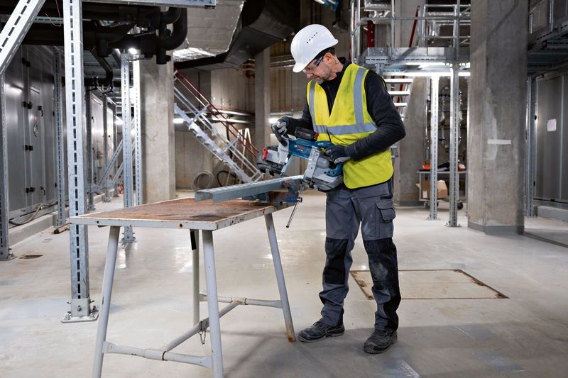 Turvavarustust kandev inimene lõikab akutoitel lintsaega metalltala.