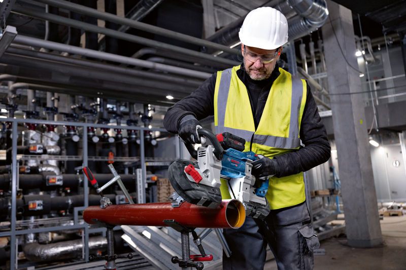 Turvavarustust kandev töötaja lõikab metalltoru akutoitel lintsaagiga.