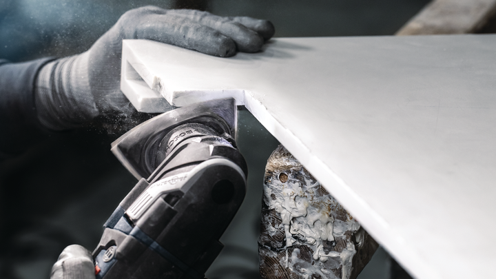 Turvavarustust kandev inimene lõikab elektrilise tööriistaga valgelt tööpinnalt nurka.