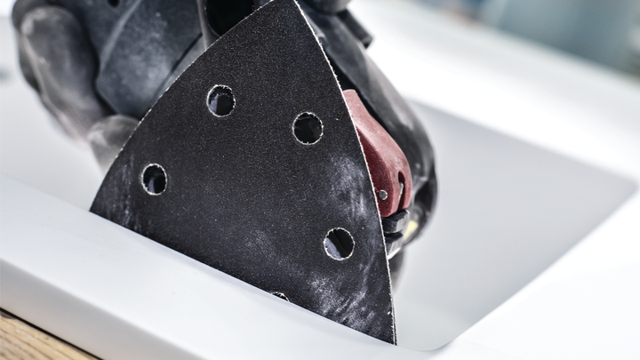 Turvavarustust kandev inimene lihvib kolmnurklihvijaga tööpinda.