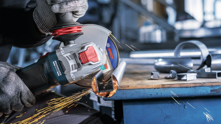 Kaitsevarustust kandev inimene krigistab metalltoru, tekitades sädemeid.