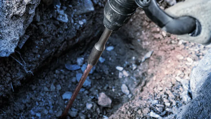 Turvavarustust kandev inimene kasutab kivide lähedal maapinda purustamiseks elektrilist tööriista.