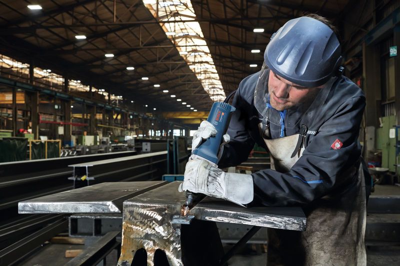 Turvavarustust kandev inimene lõikab metalltala sirglõikuriga.