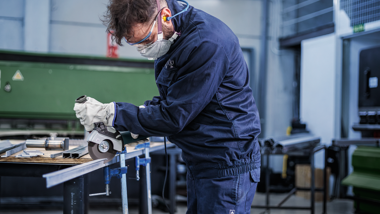 Turvavarustust kandev inimene lõikab nurklihvijaga metallvarda.