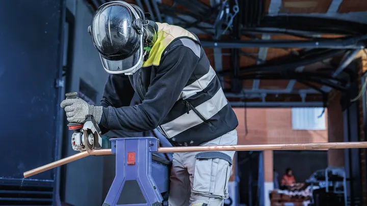 Turvavarustust kandev inimene lõikab elektrilise tööriistaga metalltoru.