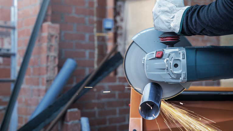 Turvavarustust kandev inimene lõikab elektrilise tööriistaga metalltoru, sädemed lendavad.