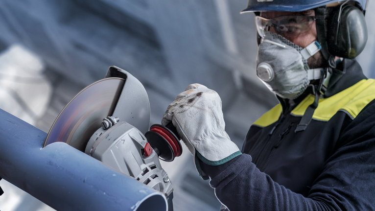 Turvavarustust kandev inimene lihvib nurklihvijaga metalltoru.