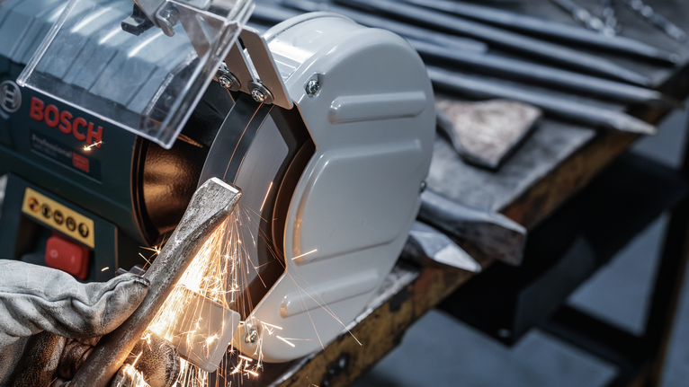 Turvavarustust kandev inimene teritab lihvimispingil metalltööriista.