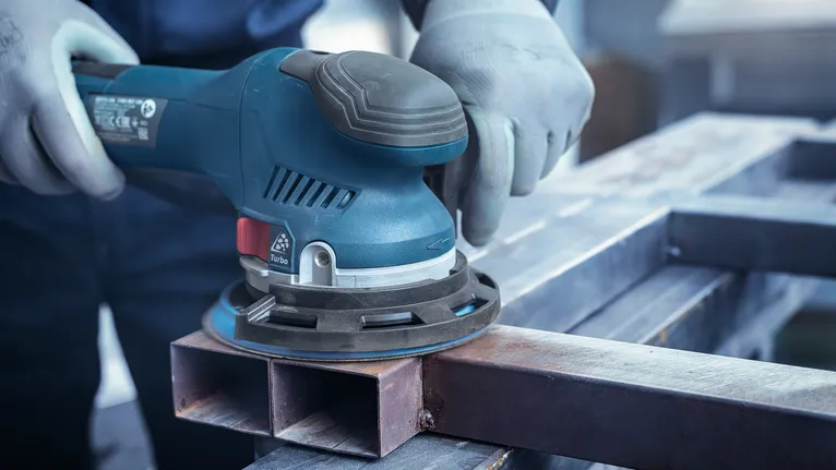 Turvavarustust kandev inimene lihvib metallpinda elektrilihvijaga.