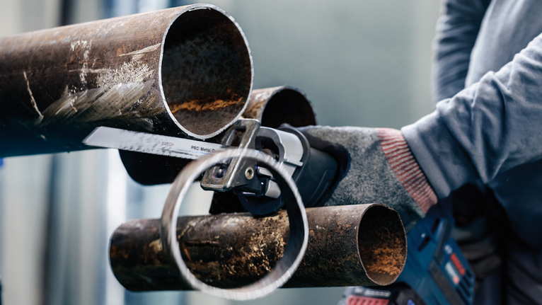 Turvavarustust kandev inimene lõikab edasi-tagasi liikuva saega metalltoru.