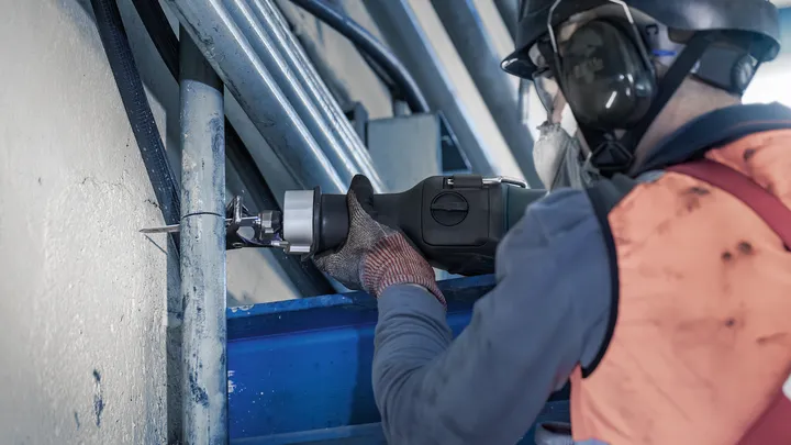 Turvavarustust kandev inimene lõikab edasi-tagasi saega metalltoru.