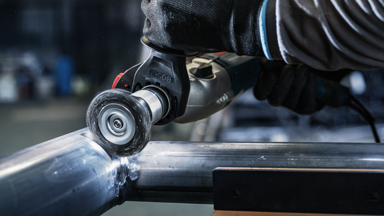 Turvavarustust kandev inimene poleerib elektrilise tööriistaga metalltoru.