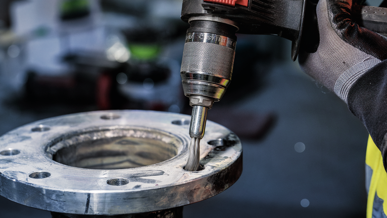 Turvavarustust kandev inimene lihvib metalltoru serva elektrilise puuriga.