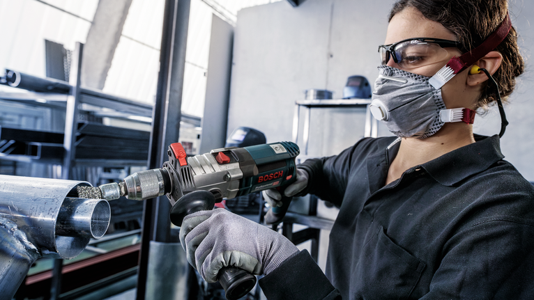 Turvavarustust kandev inimene kasutab metalltorul elektrilist puurit.