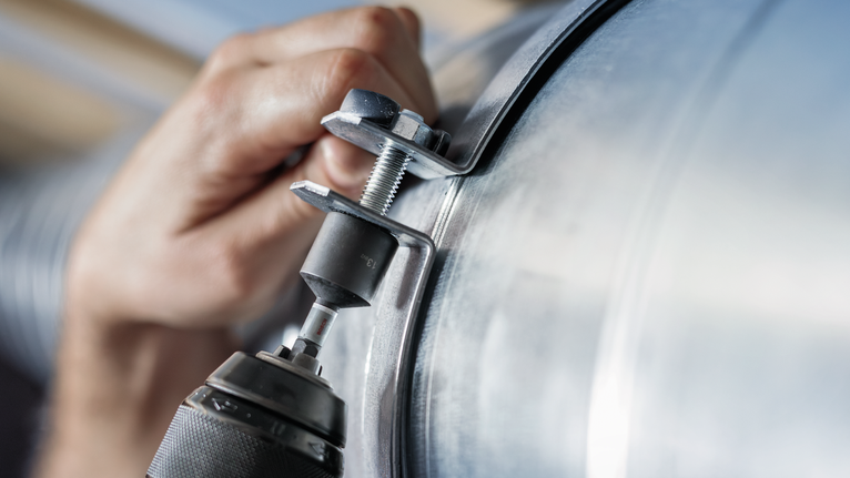 Inimene pingutab elektrilise tööriistaga polti suurele metallkanalile.