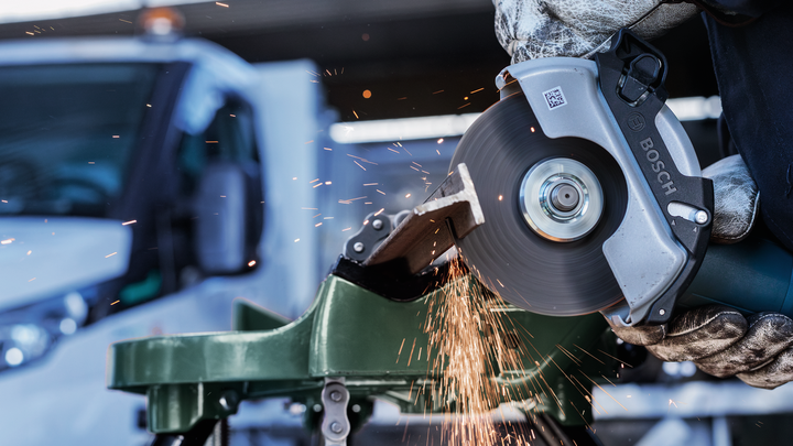 Turvavarustust kandev inimene lõikab nurklihvijaga metalltoru, sädemed lendavad.