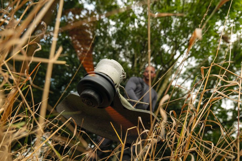 Inimene niidab metsasel alal akutoitel murutrimmeriga võsastunud muru.