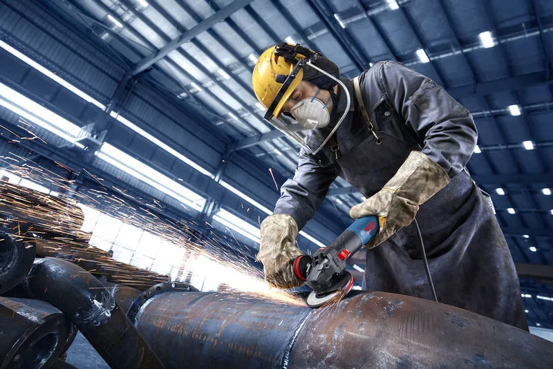 Turvavarustust kandev inimene lihvib tehases suurt metalltoru.