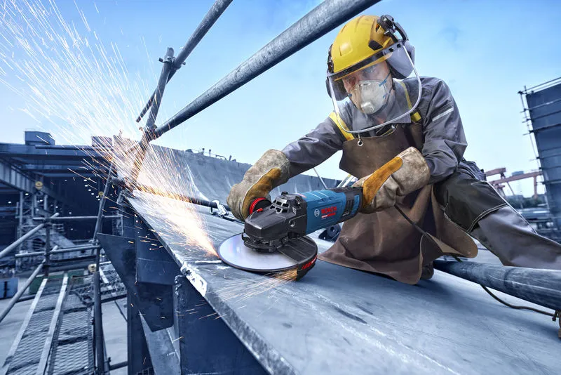 Turvavarustust kandev inimene lihvib nurklihvijaga metalltala.