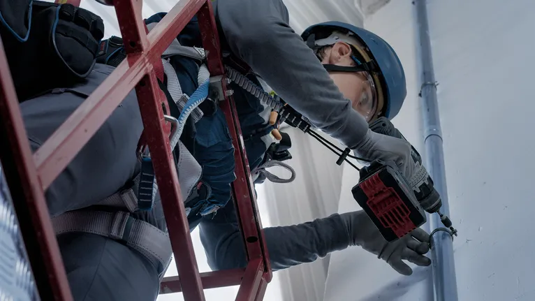 Turvavarustust kandev inimene puurib tellingu seina elektrilise tööriistaga.