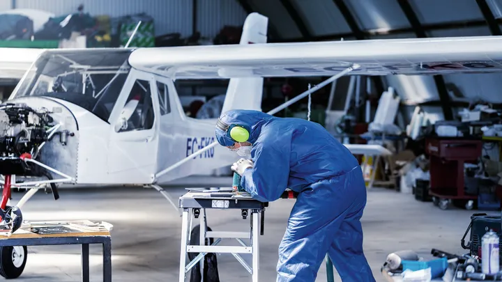 Turvavarustust kandev inimene puurib väikelennuki lähedal tööpingil metalldetaili.