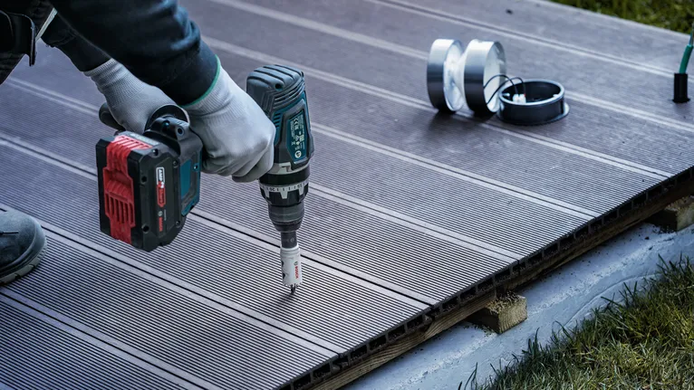 Turvavarustust kandev inimene kasutab akupuurit terrassile augu tegemiseks.