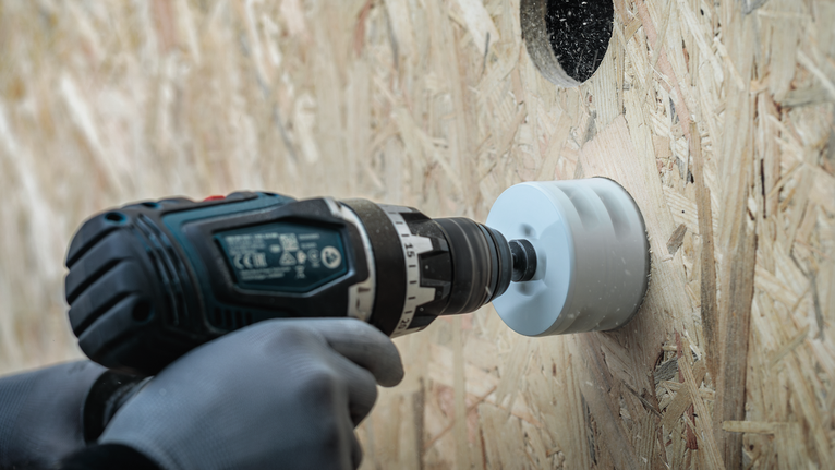 Turvavarustust kandev inimene puurib puitseina suurt auku.