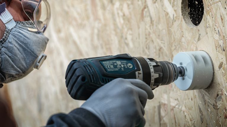 Turvavarustust kandev inimene puurib puitlauale ümmarguse augu.