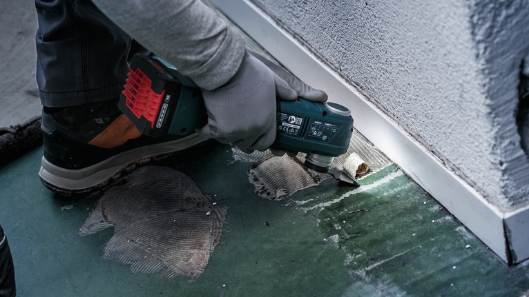 Turvavarustust kandev inimene lõikab elektrilise tööriistaga seina lähedal põrandaliimi.