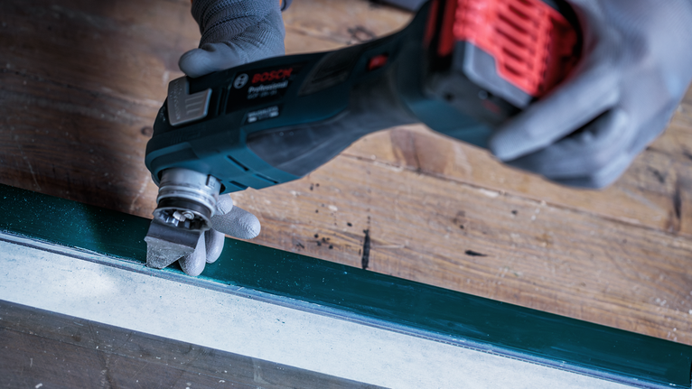 Turvavarustust kandev inimene kasutab aknaraamilt värvi lihvimiseks multitööriista.