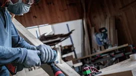 Turvavarustust kandev inimene lihvib elektrilise tööriistaga puitplanku.