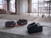 Kaks laetavat tööriistaakut ja laadija betoonpinnal ehitusplatsil.