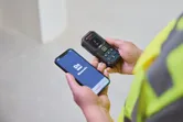 Turvavarustust kandev inimene kasutab mobiilirakendust kasutades lasermõõtjat.
