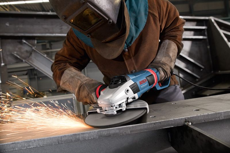 A person wearing safety equipment grinds metal, creating sparks with an angle grinder.