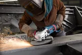 A person wearing safety equipment grinds metal, creating sparks with an angle grinder.